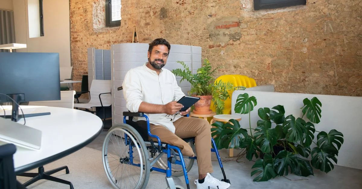 Homme d'affaires en fauteuil roulant tenant une tablette dans un cadre de bureau moderne.