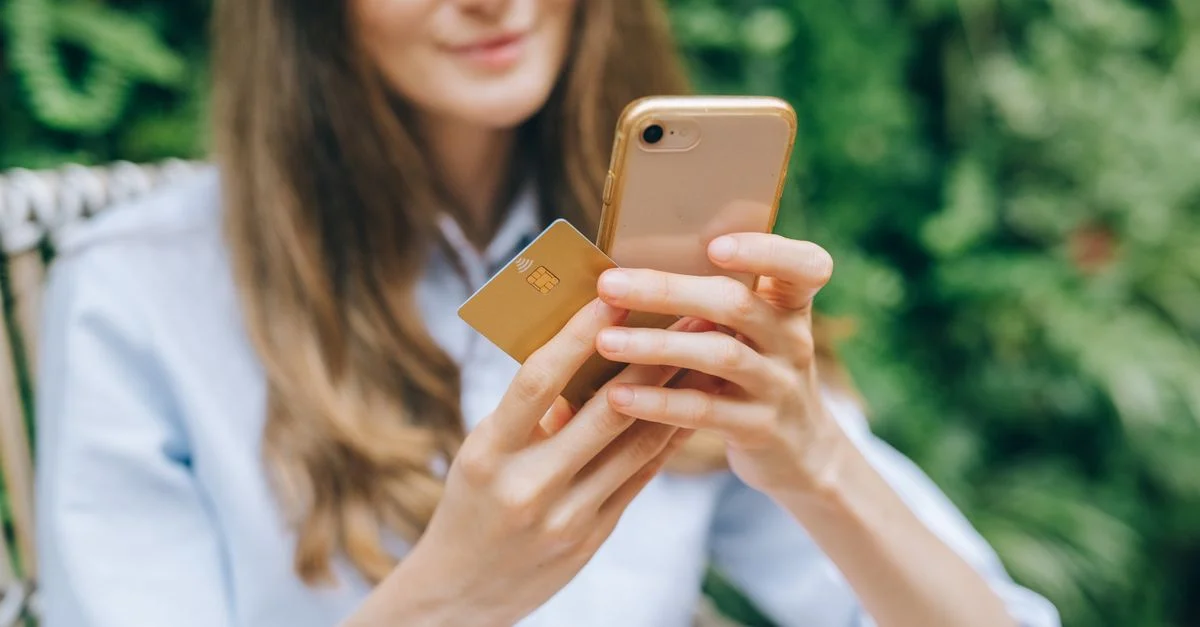 Femme utilisant un smartphone et une carte de crédit à l'extérieur pour des achats en ligne.