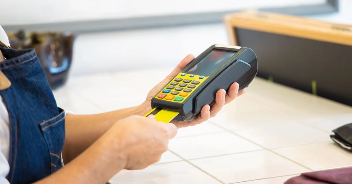 Gros plan sur des mains utilisant un terminal de paiement par carte de crédit dans un cadre commercial.