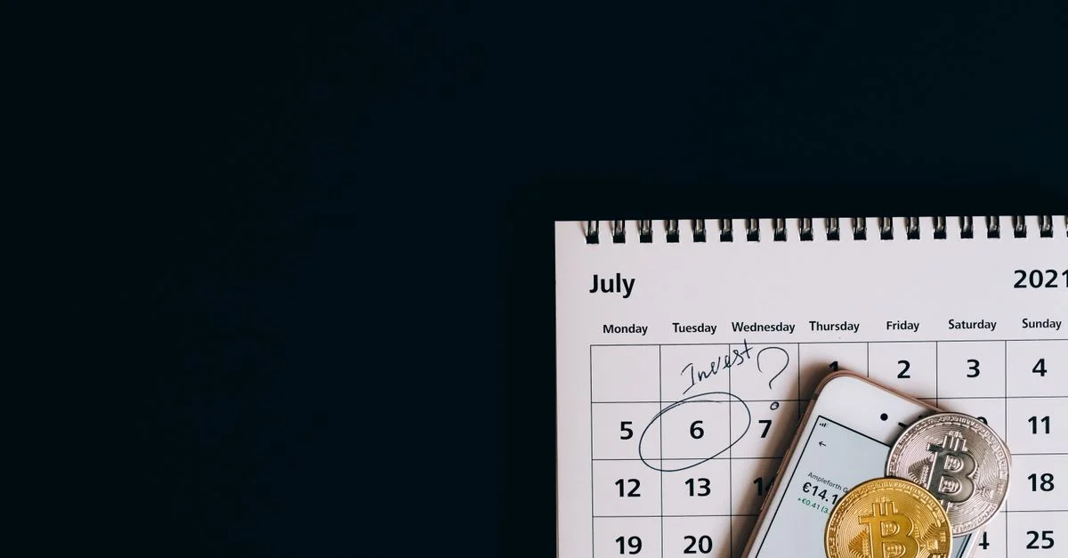 Vue de dessus de bitcoins et smartphone sur le calendrier de juillet 2021, suggérant une planification d'investissement.
