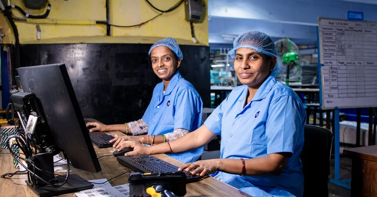 Deux ouvrières dans une usine textile utilisant des ordinateurs dans un environnement industriel.