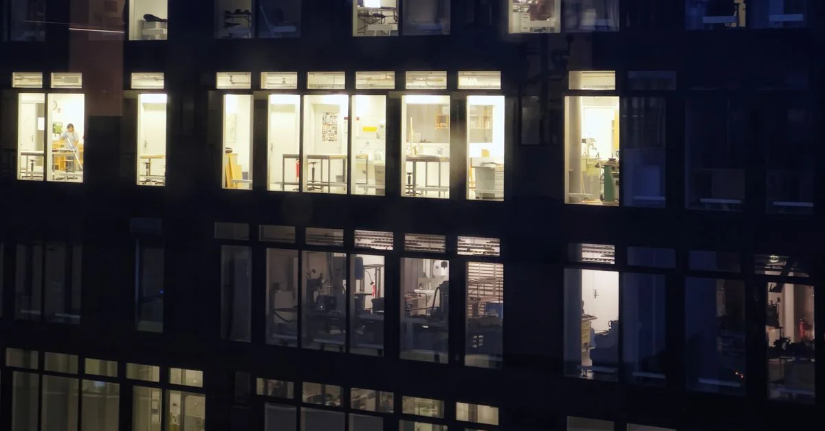 Extérieur d'un immeuble de bureaux avec des fenêtres éclairées la nuit, montrant divers espaces de travail.
