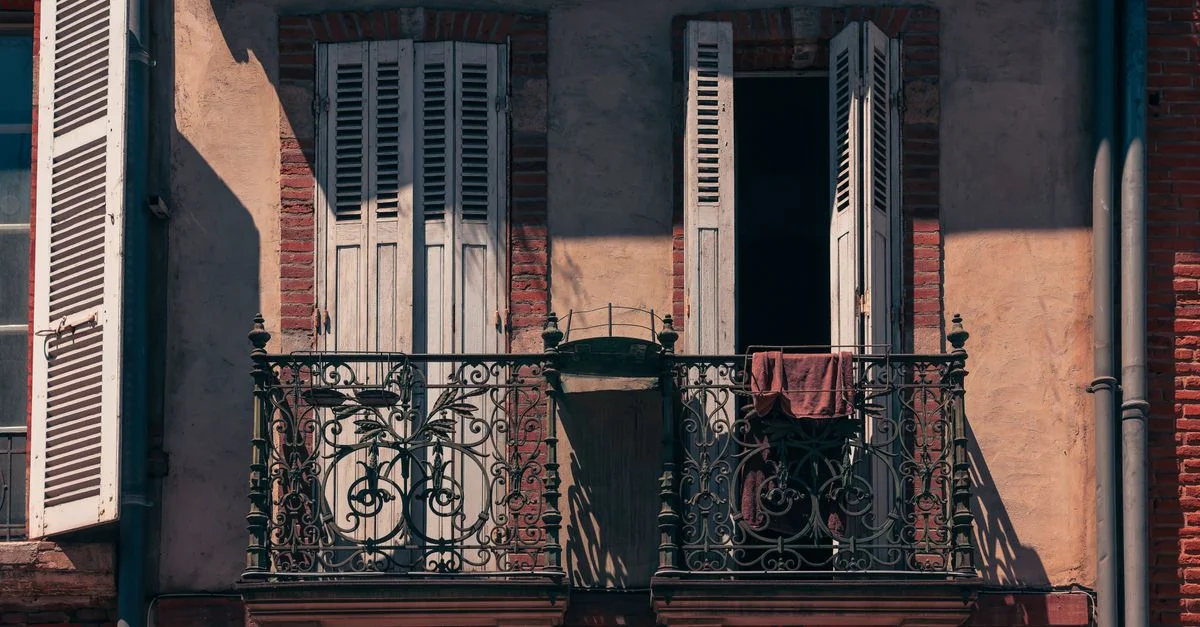 Balcon rustique avec un fer forgé complexe et des volets ouverts à Toulouse, en France, capturant l'essence de l'architecture française.