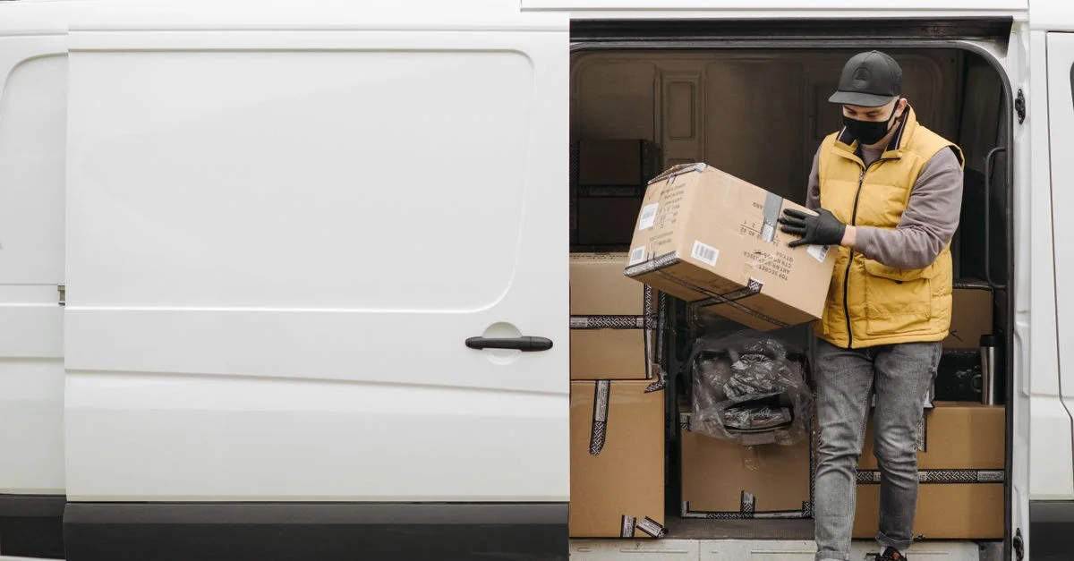 Livreur portant un masque décharge des colis d'une camionnette de livraison blanche pendant la journée.