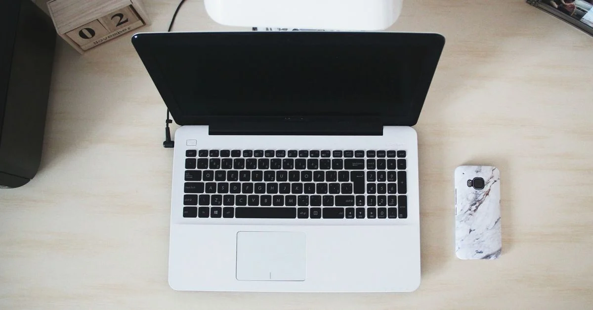 Vue de dessus d'un espace de travail minimaliste avec un ordinateur portable, un smartphone et des accessoires de bureau.