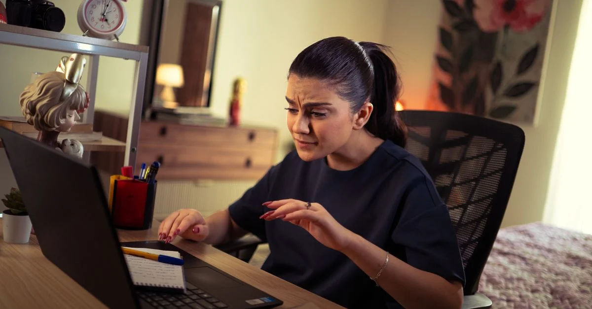 Femme concentrée sur son travail sur ordinateur portable à son bureau à domicile, entourée de fournitures de bureau.