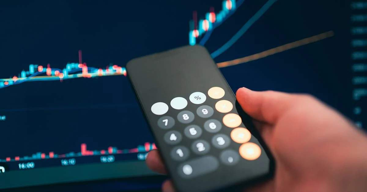 Gros plan sur un smartphone affichant une calculatrice avec un graphique financier en arrière-plan.