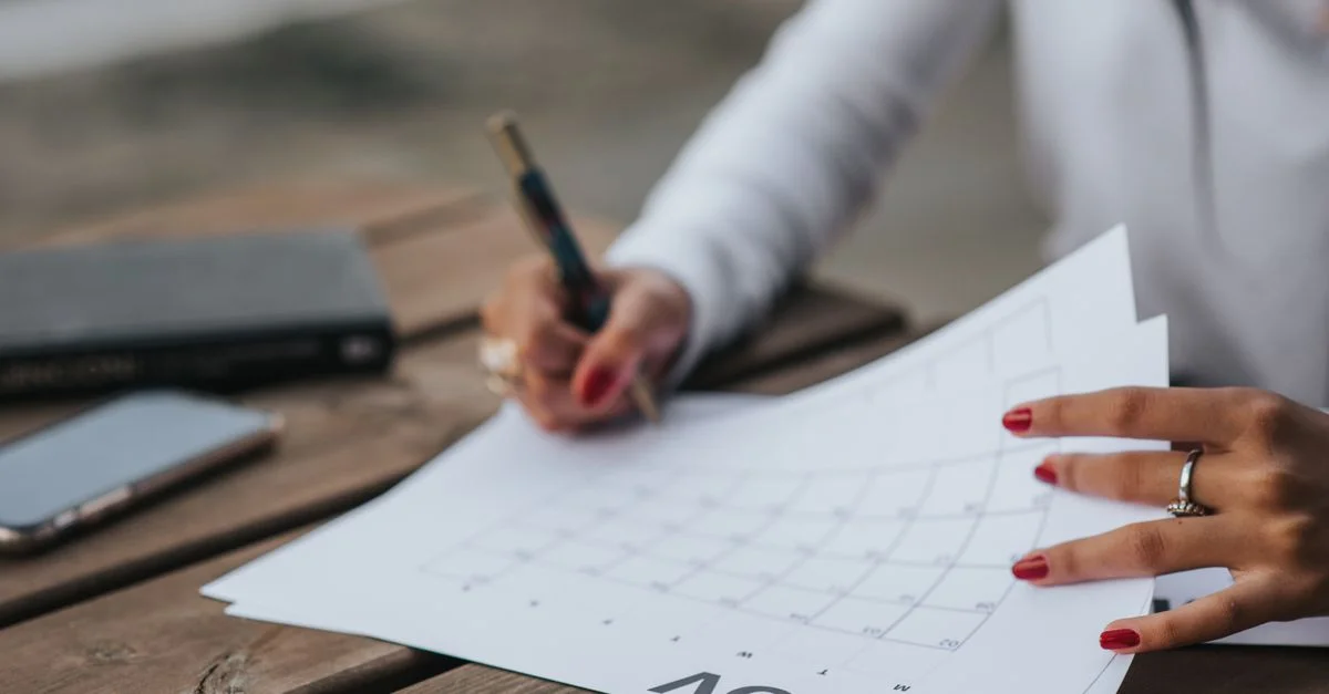 Une femme planifiant avec un calendrier en extérieur, prenant des notes sur une table en bois avec un stylo.