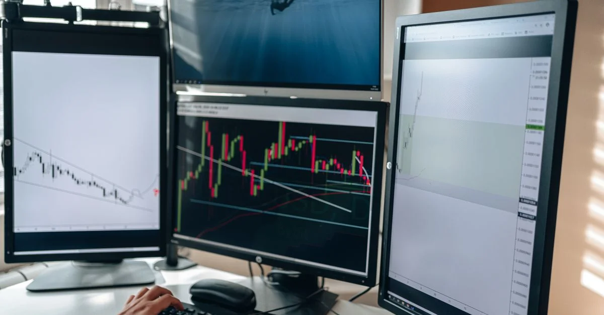 Un montage de trading en bourse avec plusieurs moniteurs présentant des graphiques et une analyse de données dans un bureau à domicile.