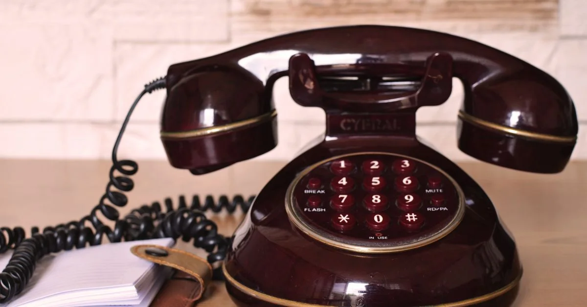 Téléphone rotatif vintage classique avec un cordon spiralé sur un bureau en bois, évoquant la nostalgie.