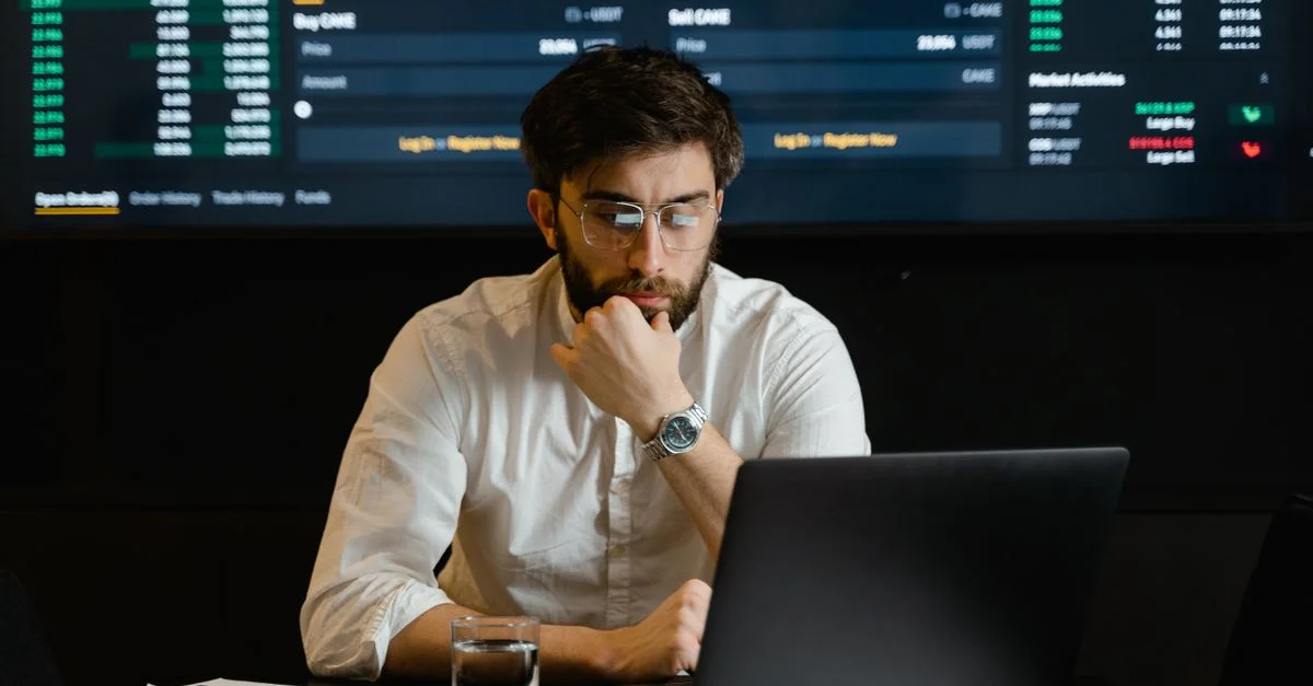 Un homme analysant intensément des données boursières sur un ordinateur portable dans un cadre de bureau.