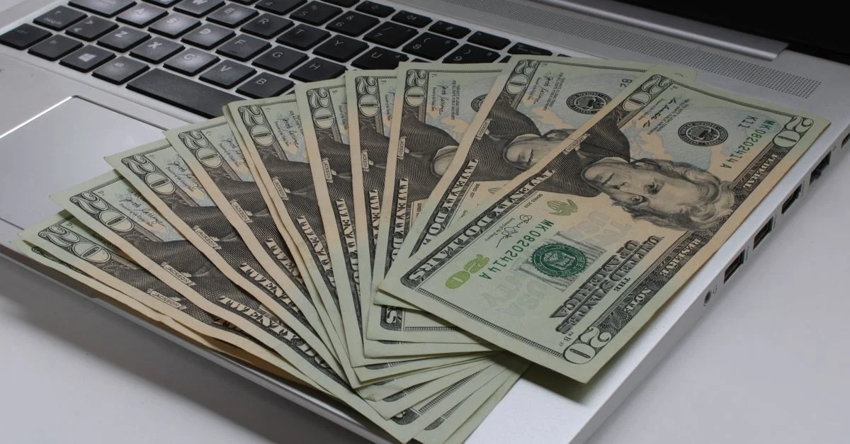 Empilement de billets de dollars américains étalés sur le clavier d'un ordinateur portable, symbolisant la finance en ligne.