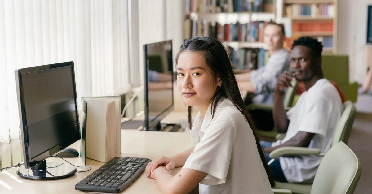Des étudiants engagés dans l'apprentissage dans une bibliothèque moderne avec des ordinateurs et un éclairage naturel.