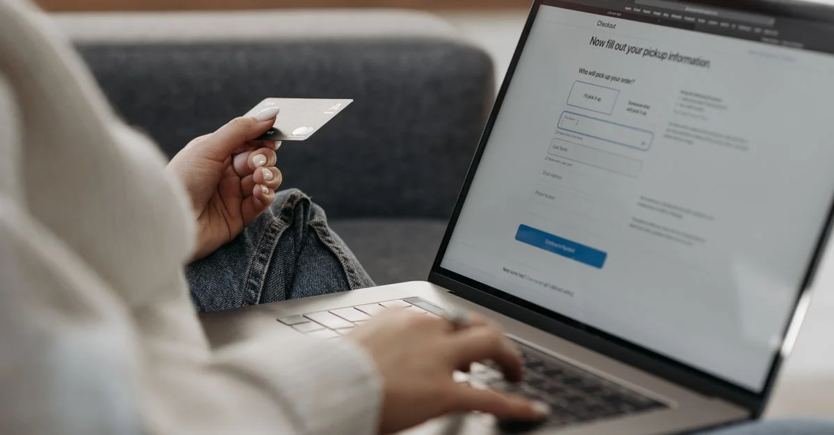 Femme utilisant une carte de crédit pour faire des achats en ligne sur un ordinateur portable depuis un canapé.