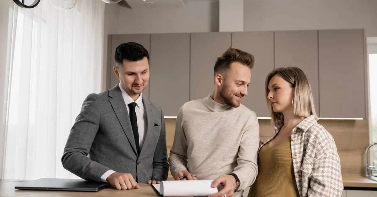 Un jeune couple discute d'un contrat immobilier avec un agent immobilier dans une cuisine moderne élégante.
