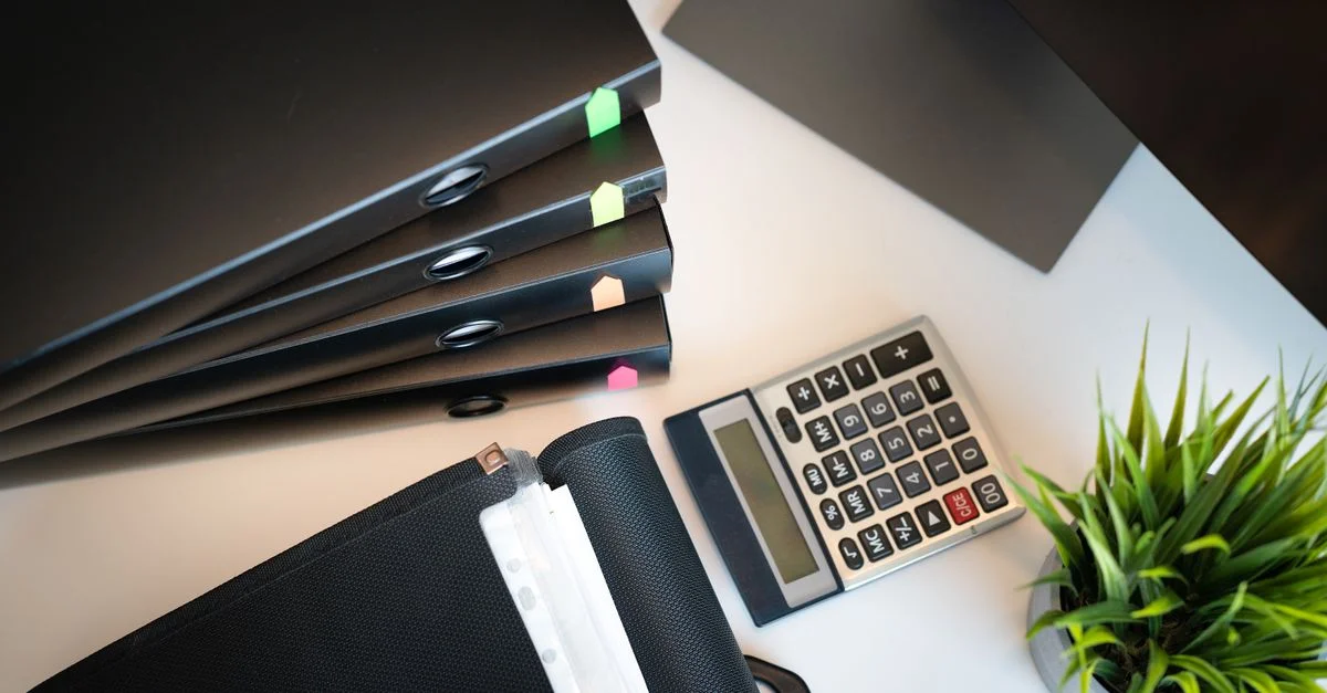 Vue de dessus d'un bureau de bureau bien rangé avec des dossiers, une calculatrice et une plante, mettant en avant l'organisation.