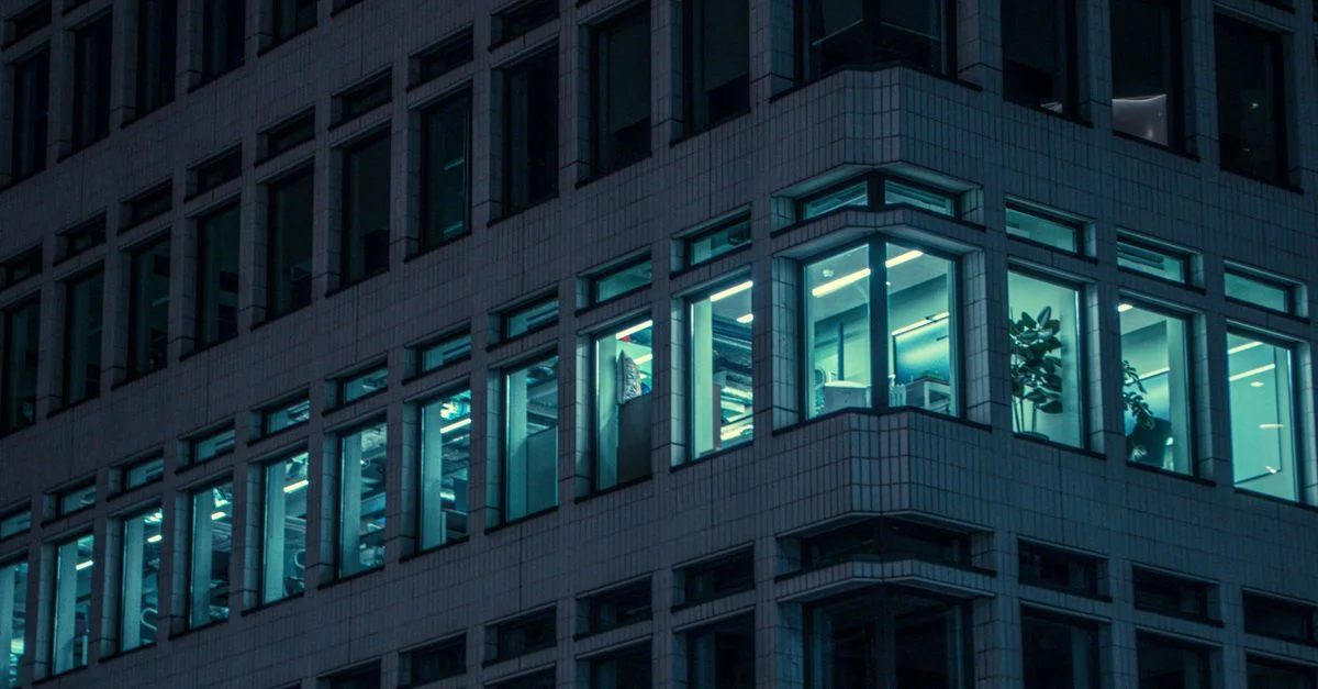 Fenêtres de bureau illumées dans un bâtiment moderne de Londres la nuit, capturant la vie urbaine.
