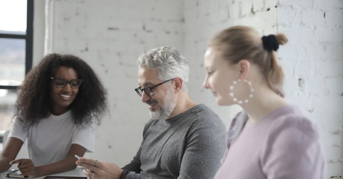 Trois collègues travaillant ensemble dans un bureau lumineux avec des appareils numériques, favorisant un environnement de travail positif.