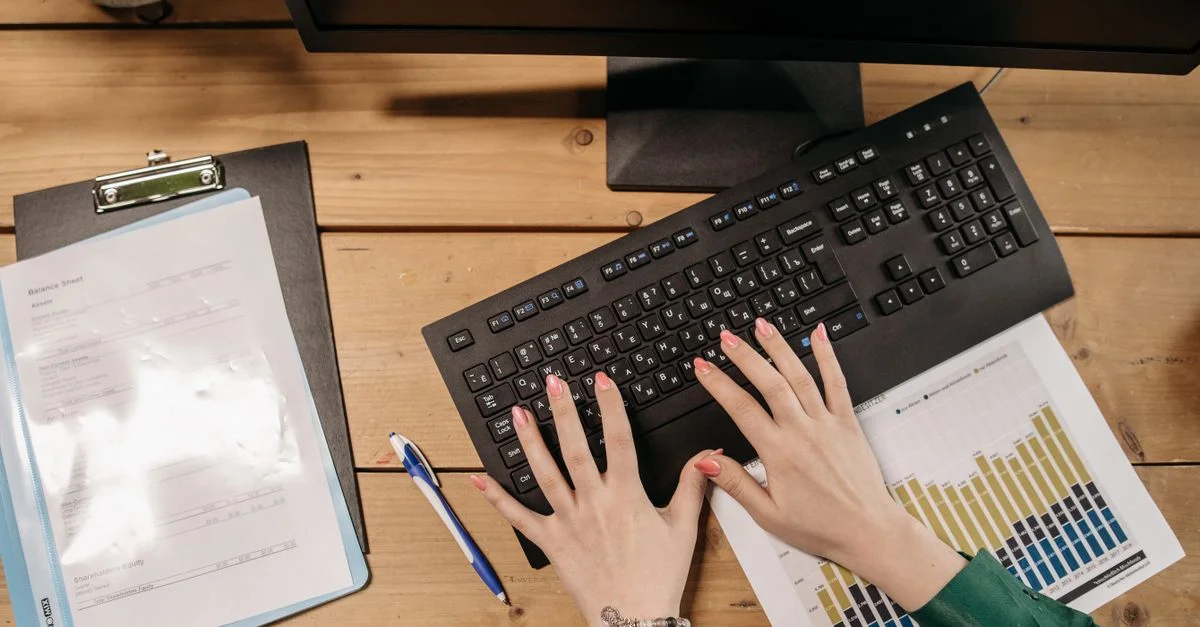 Femme tapant sur un clavier entourée de graphiques et de documents sur un bureau en bois.