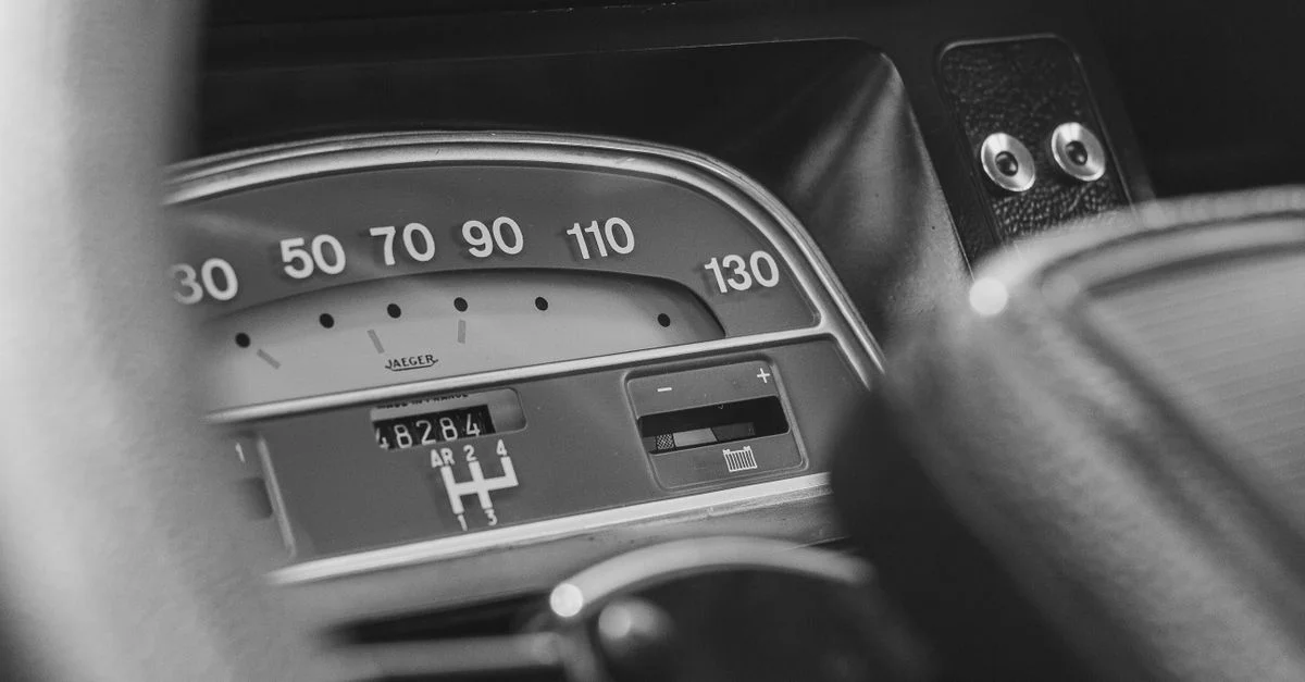 Gros plan sur le tableau de bord d'une voiture vintage en noir et blanc, mettant en avant un compteur de vitesse classique.