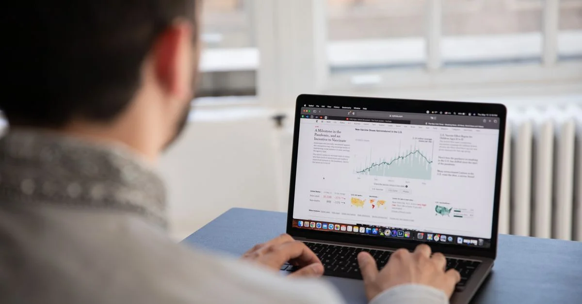 Une personne travaillant sur un ordinateur portable en analysant des données financières dans un cadre intérieur lumineux.