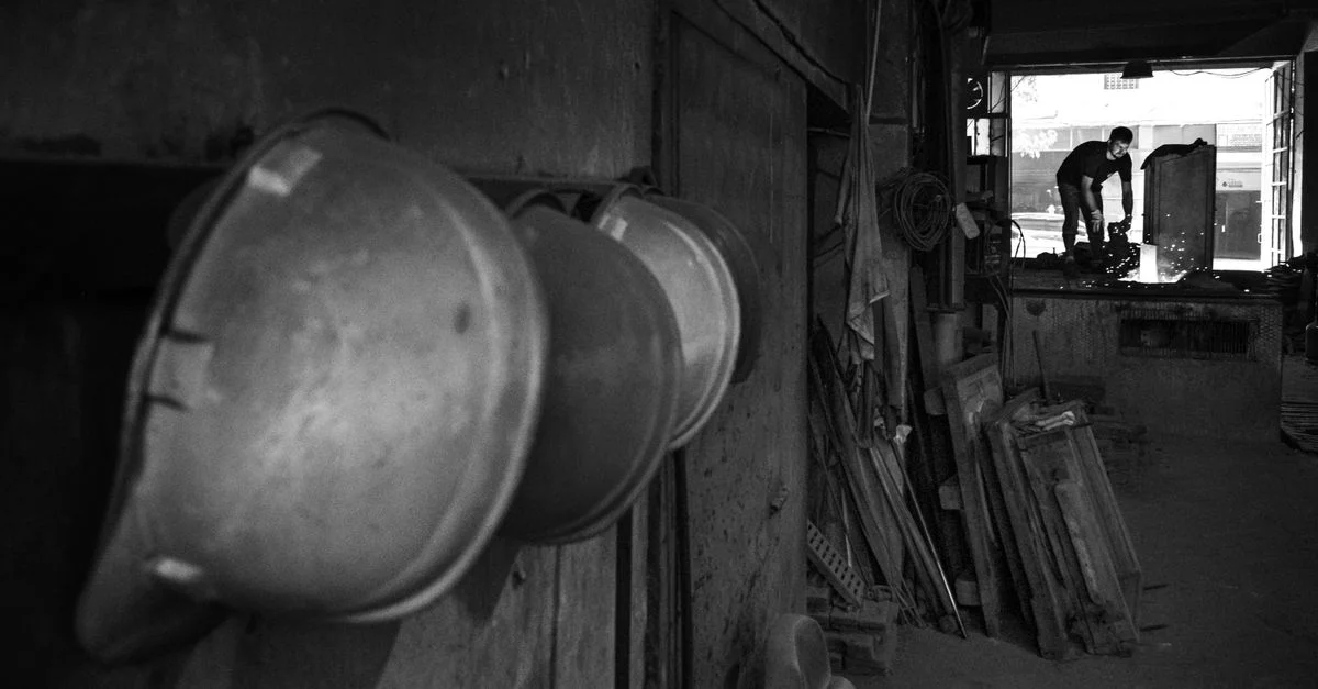 Un ouvrier soudant du métal dans un atelier industriel avec des casques de sécurité au premier plan.