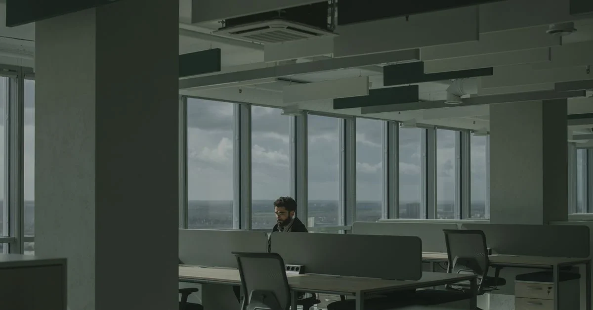 Un homme travaille seul dans un bureau moderne spacieux avec de grandes fenêtres et de la lumière naturelle.