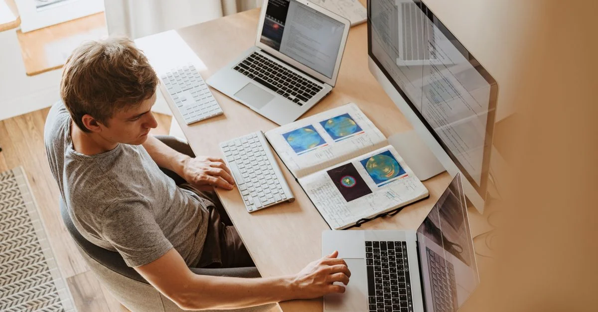 Un homme effectue plusieurs tâches avec des ordinateurs portables et un ordinateur de bureau, en train de coder dans un bureau à domicile.