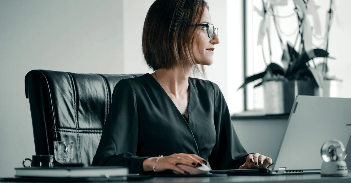 Femme adulte travaillant à un bureau avec un ordinateur portable, des lunettes et une chaise en cuir.