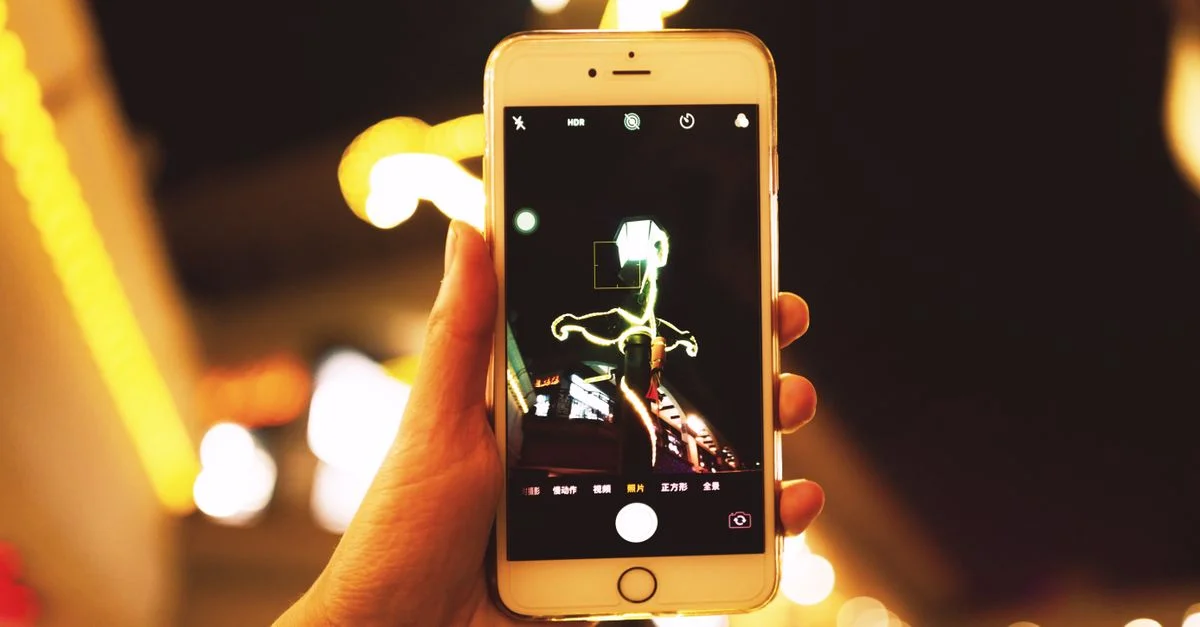 Main tenant un smartphone capturant les lumières de la ville la nuit. Parfait pour des thèmes urbains et technologiques.