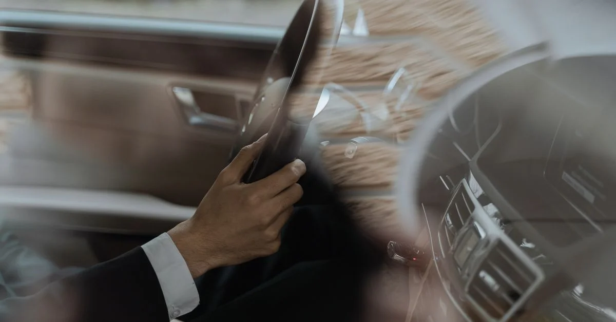 Gros plan sur la main d'un conducteur sur le volant d'une voiture de luxe, pris à l'intérieur du véhicule.