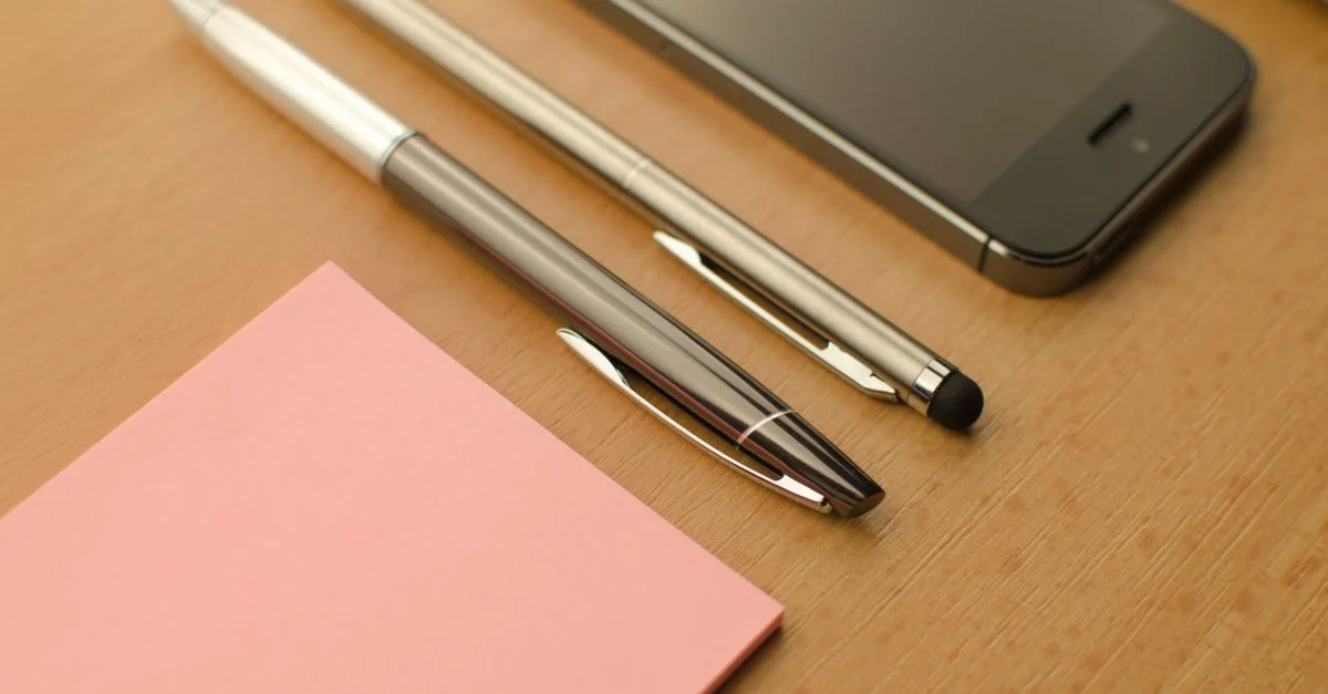 Espace de travail élégant avec un smartphone, des stylos et un bloc-notes sur un bureau en bois.