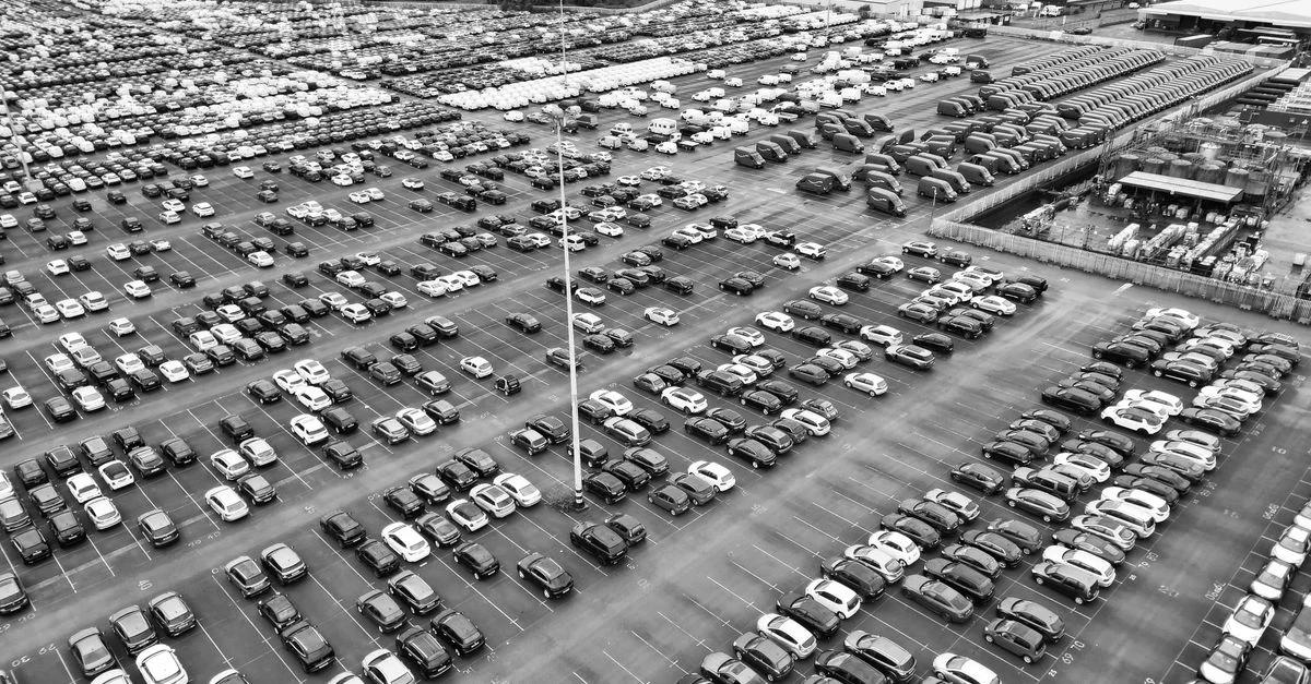 Vue aérienne en noir et blanc d'un vaste parking en Angleterre, mettant en valeur l'urbanisme.