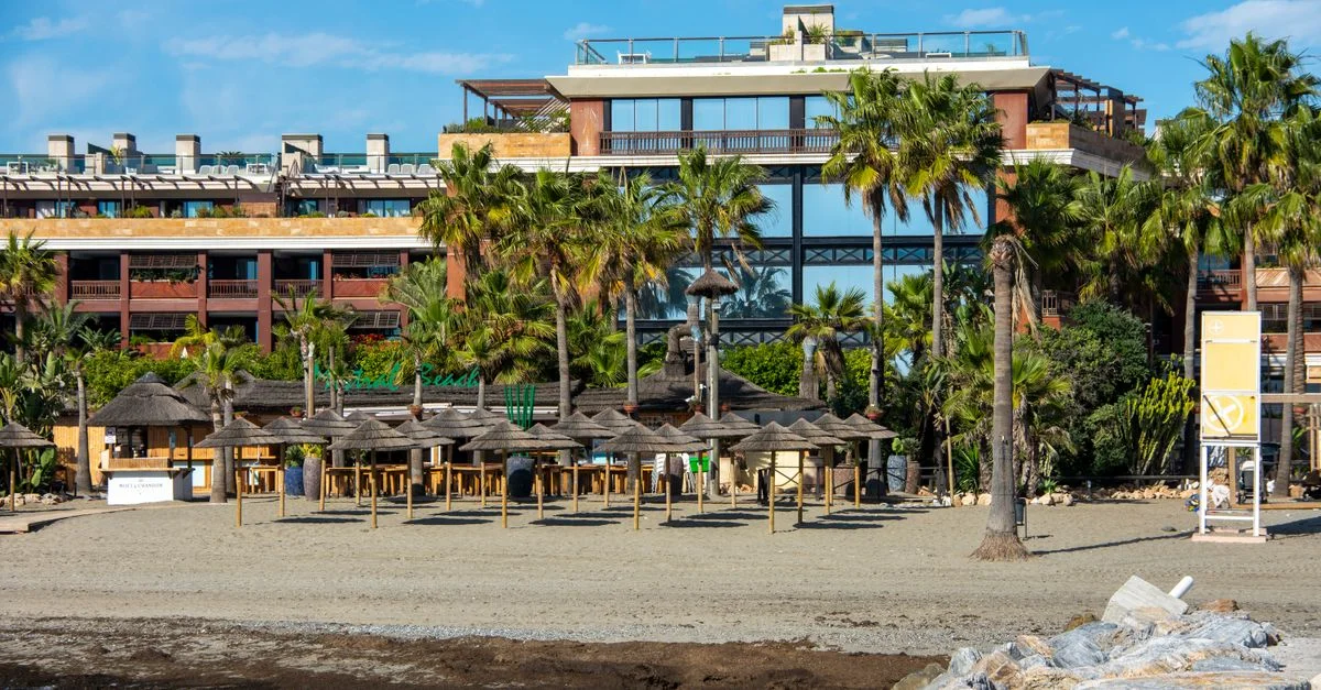 Vue pittoresque d'un bâtiment en bord de mer avec des palmiers et des cabanes de plage à Marbella, en Espagne.