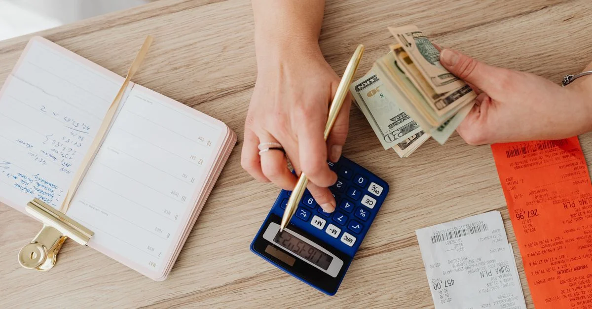 Mains gérant les finances avec une calculatrice, de l'argent liquide et des reçus sur une table en bois. Idéal pour des concepts de budgétisation.