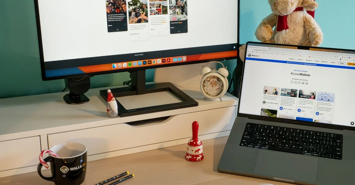 Un bureau cosy aux thèmes de Noël avec un ordinateur portable, un moniteur et des décorations de fête.