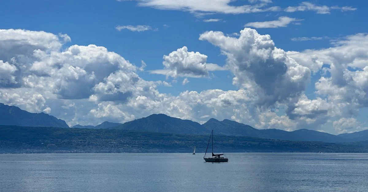 Scène tranquille de bateaux naviguant sur le lac Léman sous un ciel vibrant avec des montagnes en arrière-plan.