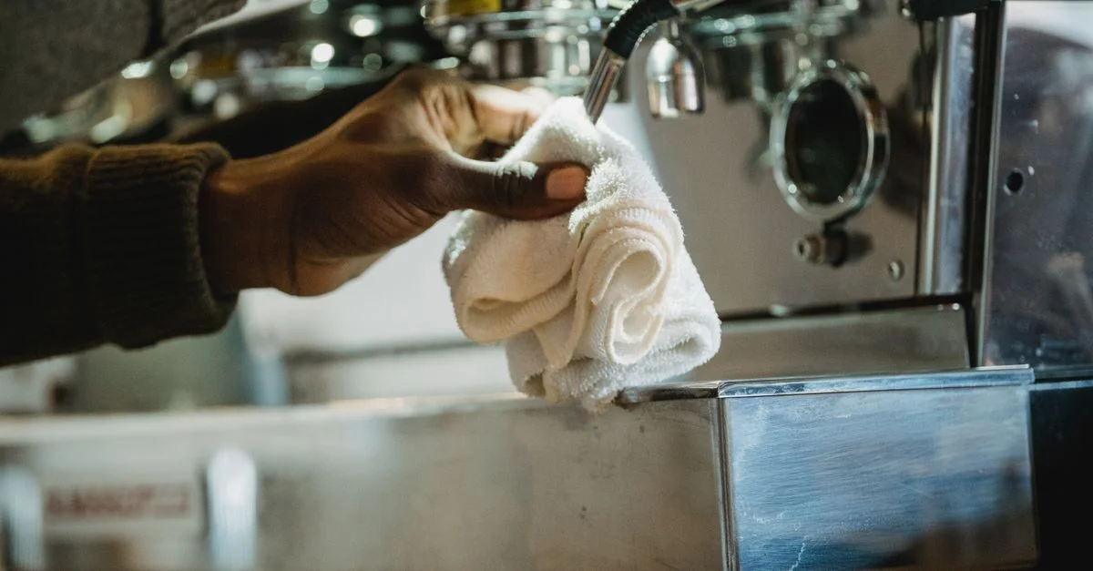 Gros plan d'une personne nettoyant une machine à café avec un chiffon. Accent sur l'hygiène et l'entretien.