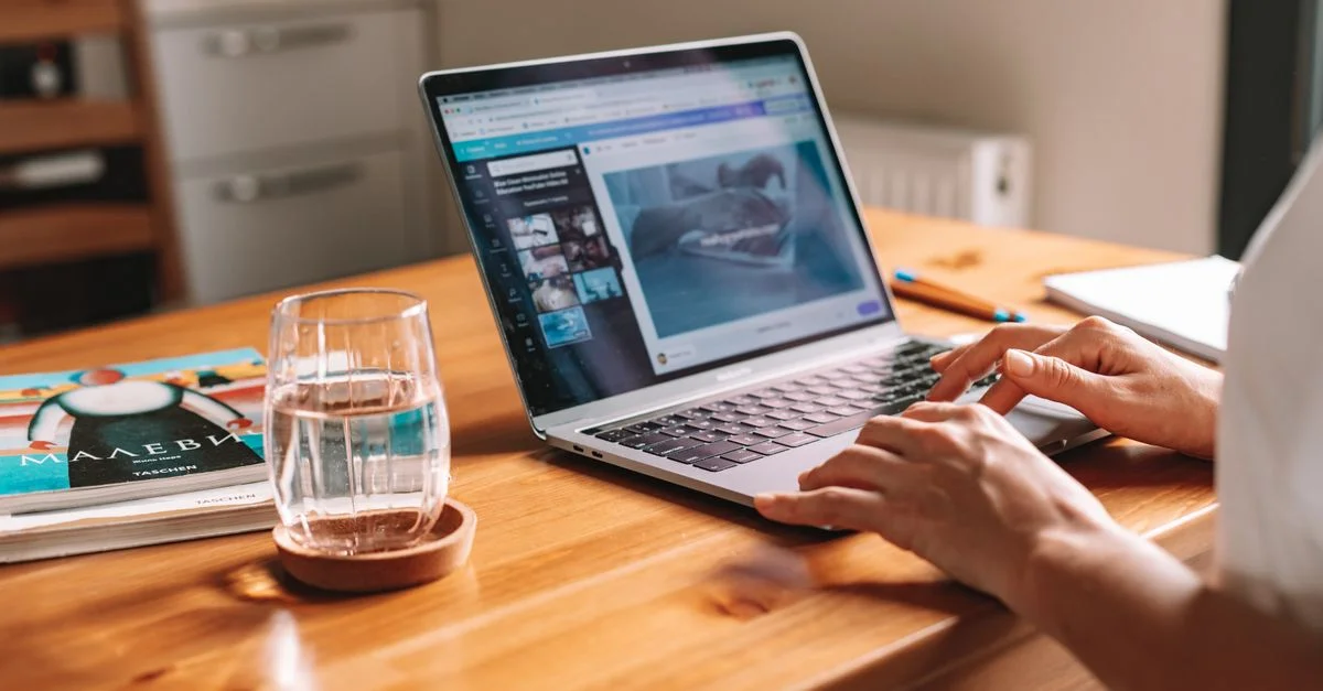 Gros plan des mains sur un ordinateur portable dans un bureau à domicile confortable avec un verre d'eau sur le bureau.
