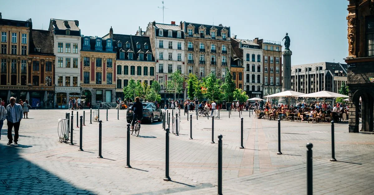 Place ensoleillée à Lille, France avec des bâtiments historiques et des cafés animés.