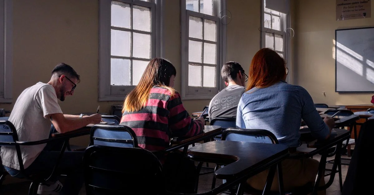 Des étudiants prennent des notes attentivement dans une salle de classe bien éclairée par la lumière naturelle.