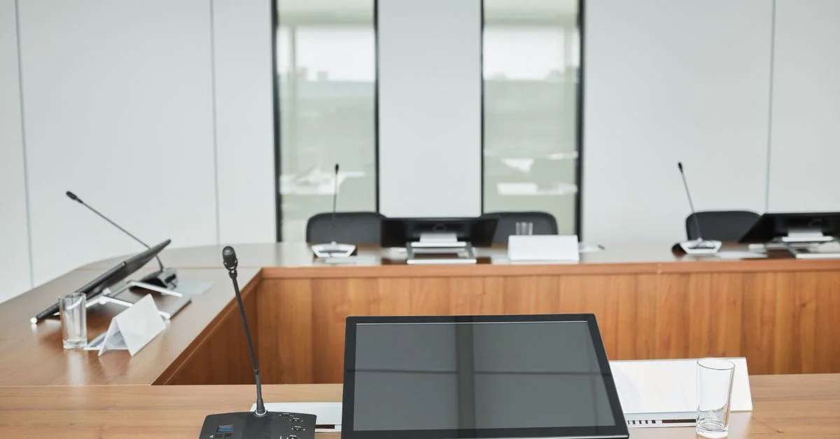 Salle de conférence vide équipée de microphones, de moniteurs et de tables en bois élégantes prêtes pour les réunions.
