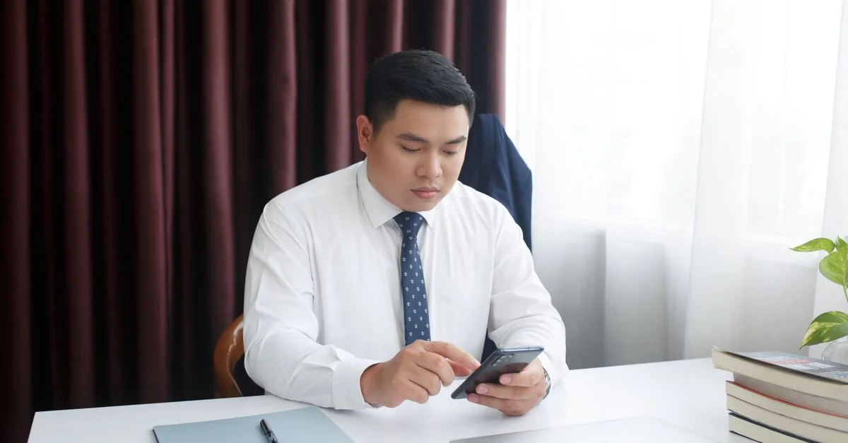 Un homme d'affaires en chemise blanche et cravate utilisant un smartphone à un bureau.