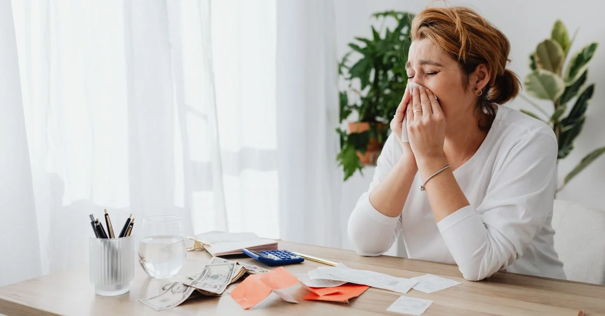 Femme stressée gérant ses finances à son bureau avec des papiers et une calculatrice.