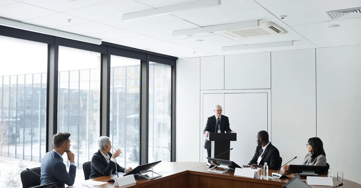 Réunion d'entreprise avec des professionnels divers écoutant un conférencier au podium dans une salle de conférence moderne.