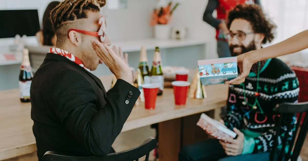 Groupe d'adultes profitant d'une fête de vacances avec des pulls festifs, des cadeaux et des boissons à l'intérieur.