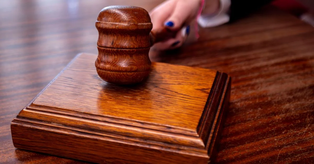 Gros plan sur un maillet de juge en bois posé sur un bureau dans une salle d'audience, symbolisant la justice.