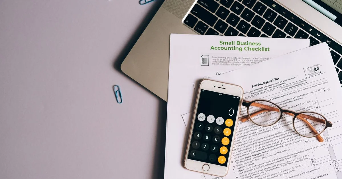 Vue de dessus des outils comptables d'une petite entreprise, y compris un formulaire fiscal, un téléphone et des lunettes sur un bureau.