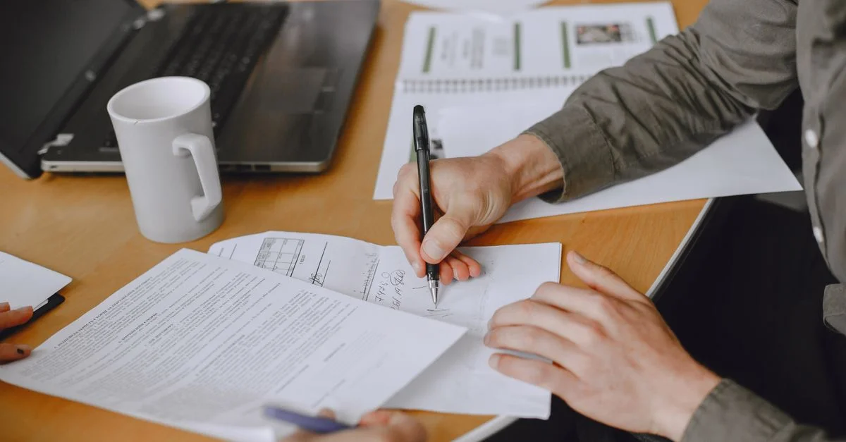 Gros plan sur des individus signant des documents lors d'une réunion d'affaires avec un ordinateur portable sur une table.
