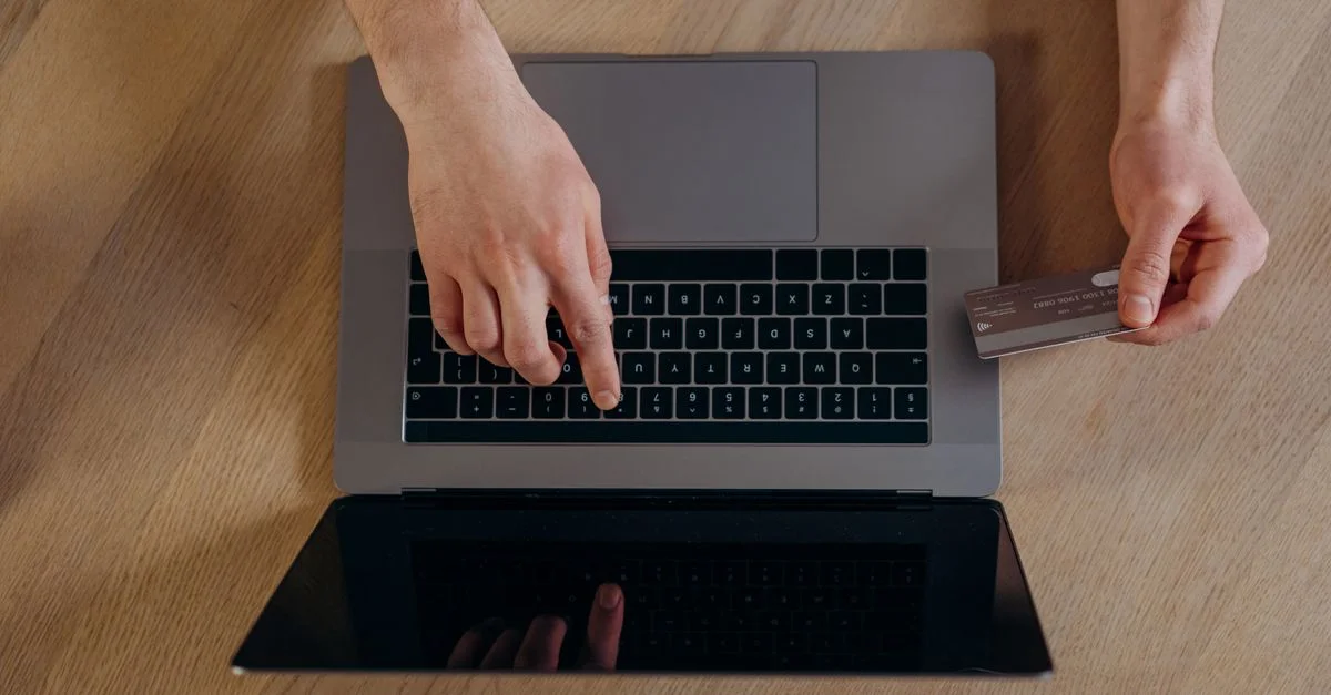 Vue de dessus des mains utilisant une carte de crédit et un ordinateur portable pour des transactions en ligne sur une surface en bois.